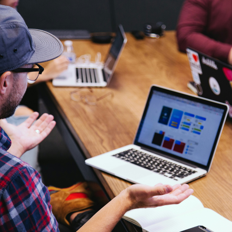 a man talking at a table with an Apple Macbook