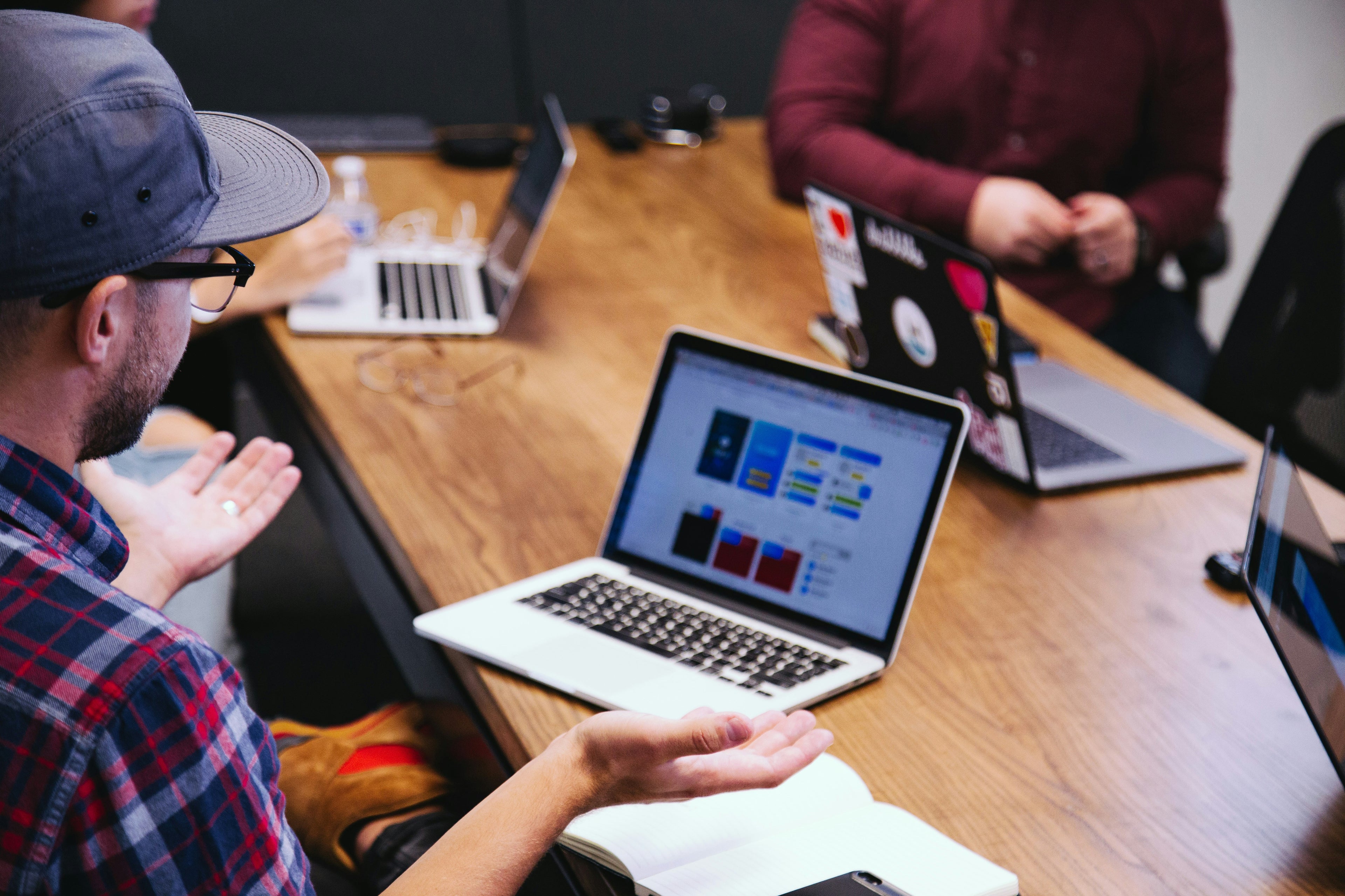 a group of people sitting around a table using Apple computers